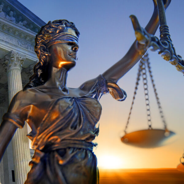 A statue of the blindfolded lady justice in front of the United States Supreme Court building as the sun rises in the distance symbolizing the dawning of a new era.